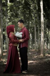 Side view of romantic young couple looking at each other while standing against trees in forest