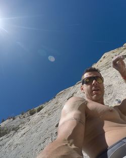 Low angle portrait of mature man standing by rock formation against clear blue sky