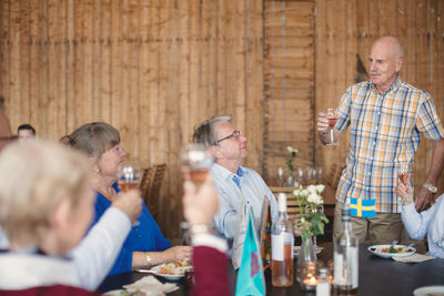Senior man toasting drink to friends at table in restaurant