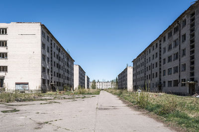 Empty road amidst buildings against clear blue sky