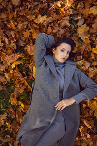 Brunette woman in a gray coat and boots it lies on the foliage in autumn. orange foliage