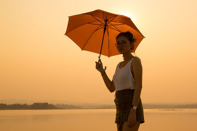 Portrait of woman with umbrella standing against lake