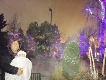 Portrait of smiling young woman with illuminated trees against sky at night