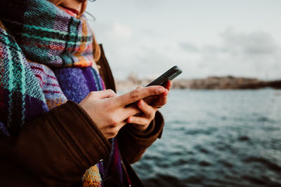 Midsection of woman using mobile phone by lake