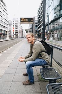 Portrait of young man sitting on sidewalk in city