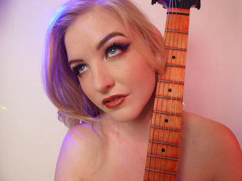 Close-up of young woman playing guitar against wall