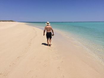 Rear view of shirtless man walking on shore at beach against sky during summer