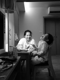 Happy mother and daughter sitting on table at home