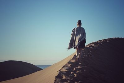 Rear view of woman walking on sand against clear sky