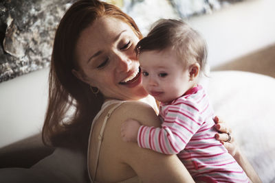 Happy mother embracing daughter while sitting on sofa at home