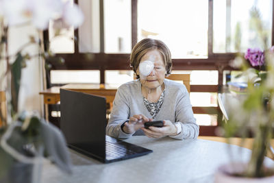 Injured senior woman using smart phone at table in home