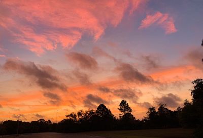 Silhouette trees on field against dramatic sky during sunset