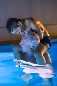 Grandfather and grandson playing in a swimming pool at night