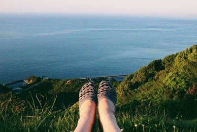 Low section of woman on grassy hill against sea