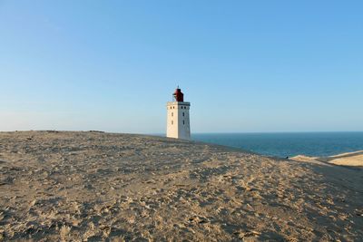 Lighthouse on beach against clear sky