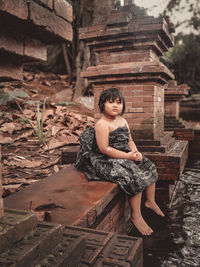 Portrait of young woman sitting on wooden wall