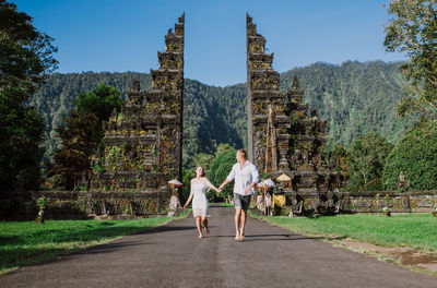 Couple running on footpath at gate against sky