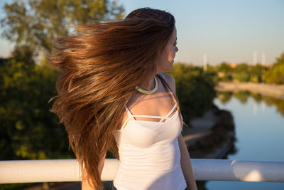 Young woman with tousled hair standing by railing over river