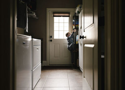 Side view of carefree boy climbing on rack at home seen through doorway