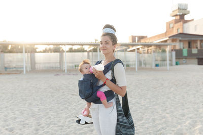 Mother feeding milk to daughter while standing at beach