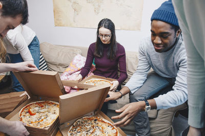 High angle view of young friends opening pizza boxes in dorm room