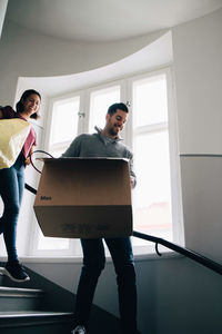 Low angle view of couple carrying box and bag while moving down steps