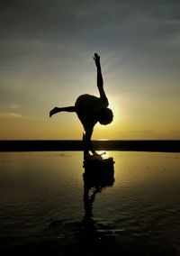Silhouette man jumping at sea against sky during sunset