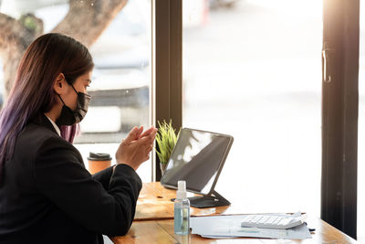 Side view of businesswoman wearing mask using hand sanitizer at office