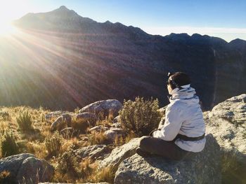 Rear view of woman sitting on rock against sky