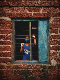 View of woman looking through window on brick wall
