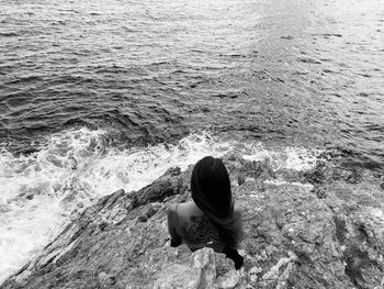 Rear view of woman sitting on rock in sea