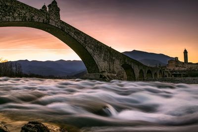 Bridge over river against sky during sunset