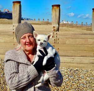 Portrait of woman holding dog while standing at beach