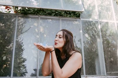 Young woman blowing origami crane by greenhouse