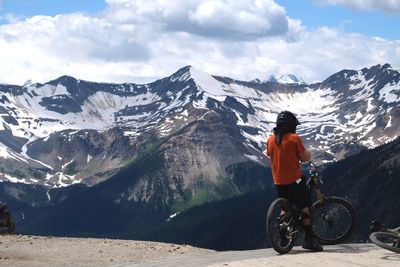 Man cycling on snowcapped mountains against sky