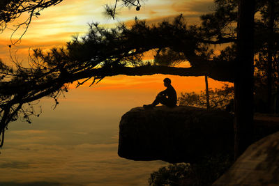 Man sitting on rock against orange sky