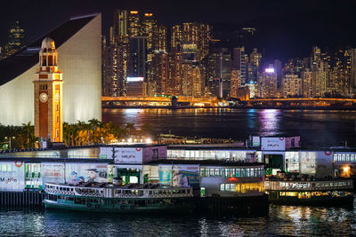 Illuminated modern buildings by river against sky in city at night