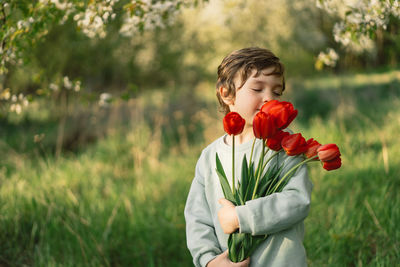 Cheerful happy child with tulips flower bouquet in nature.