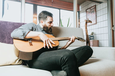 Young man playing guitar while sitting on sofa at home