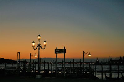 Street lights on pier by sea against sky at sunset