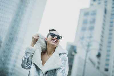 Low angle view of cheerful woman wearing warm clothing in city