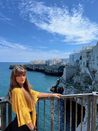 Portrait of young woman standing by sea against sky