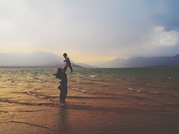 Woman standing on beach against sky during sunset