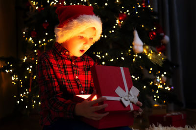 Portrait of young woman using digital tablet while standing against illuminated christmas tree