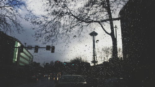 Cars on street by building against sky during monsoon seen through wet windshield