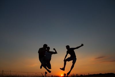 Cheerful men jumping over field against sky during sunset