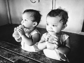 Cute siblings drinking milk from bottles at home