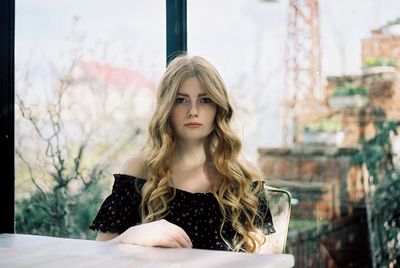 Portrait of beautiful young woman sitting against window