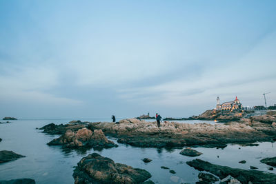 People on rocks by sea against sky