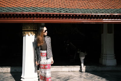 Portrait of young woman standing against building